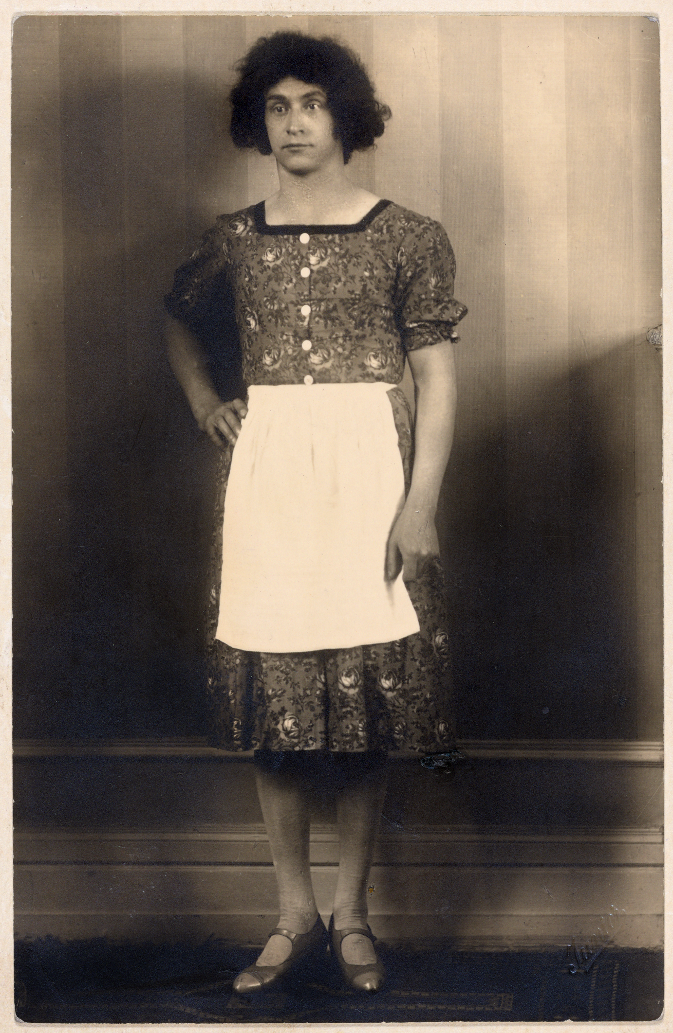 The young Hertha Wind in a dirndl with an apron and medium-long hair in front of a wallpapered wall in an apartment.