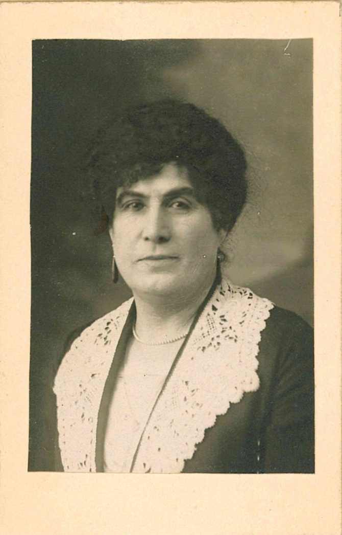 portrait photo of Emilie Kellner, short dark curly hair, small peal neclace and earrings, dark dress with big white lace collar.