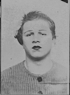 Mugshot of _Breitling, wearing a wool vest, lipstick, eyebrows drawn, short disheveled hair.