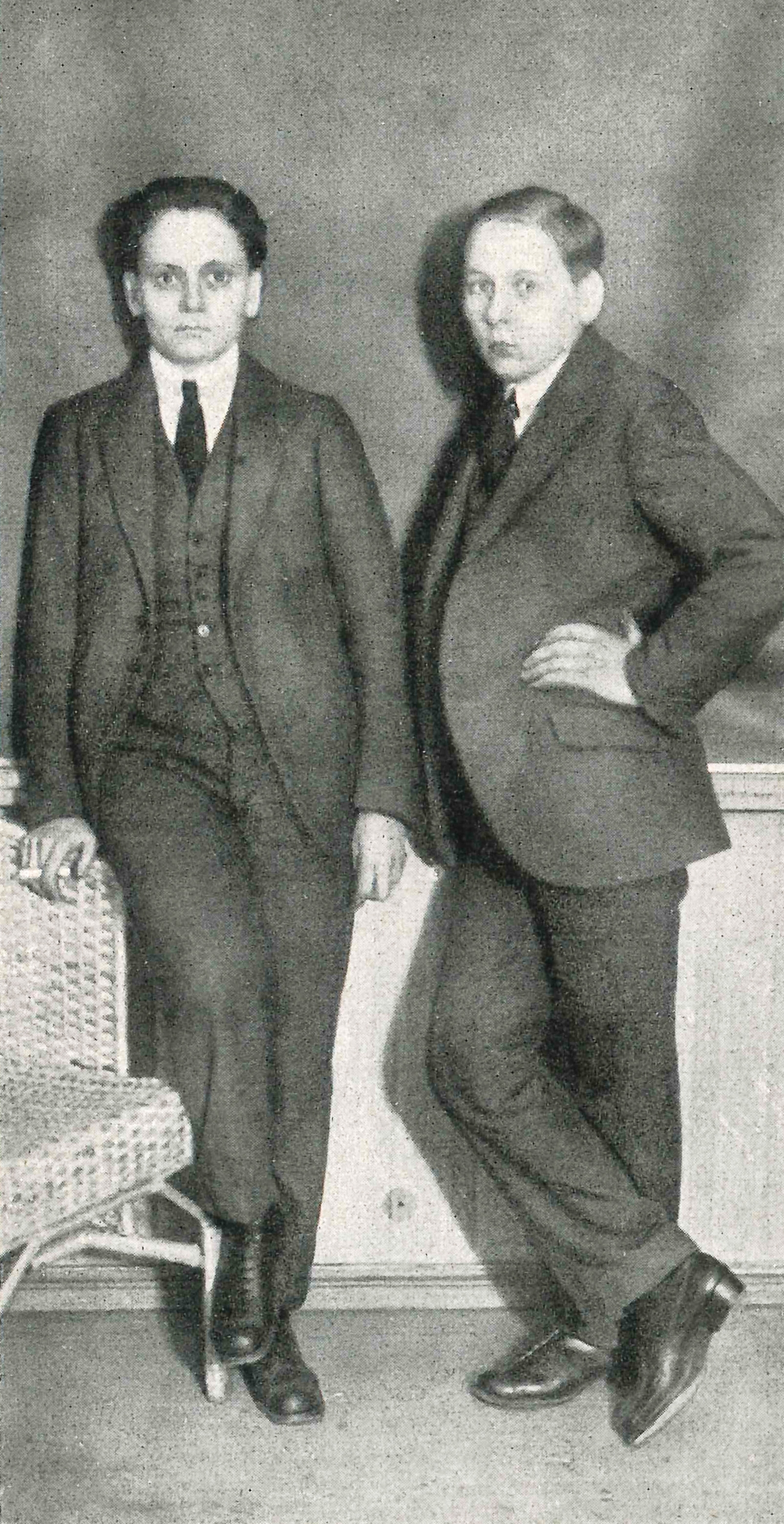 Both wear suits, ties and vests. They lean against a wall, _Gehse with his back and holds a cigarette in his right hand, which he rests on a wicker chair, *Gert Liehr with his right shoulder to the side, with his left hand on his hip.